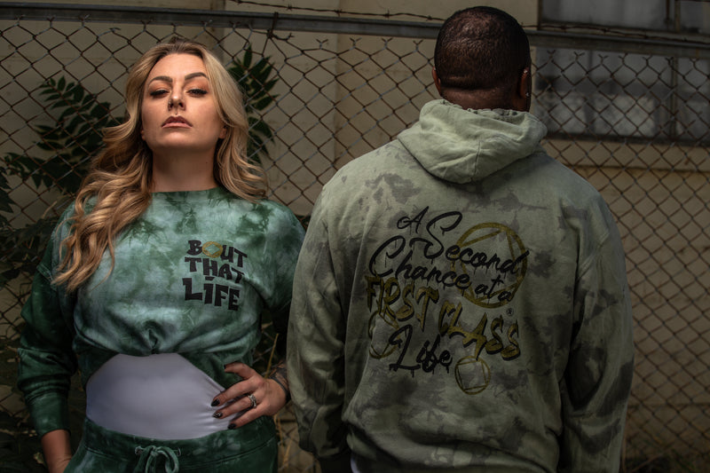 Load image into Gallery viewer, Two people wearing tie-dye shirts with text, standing in front of a chain-link fence.