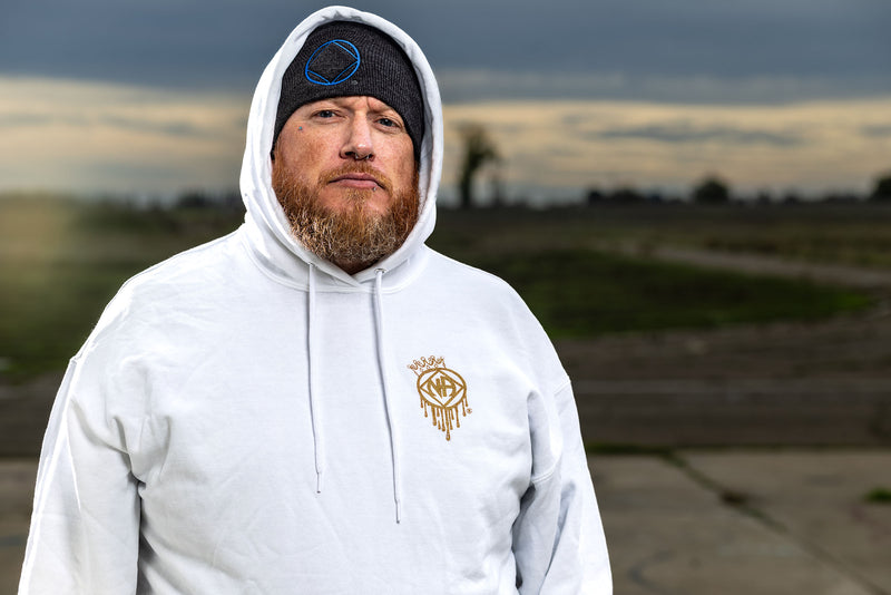 Load image into Gallery viewer, Man wearing a white hoodie with a logo, standing outdoors with a blurred background