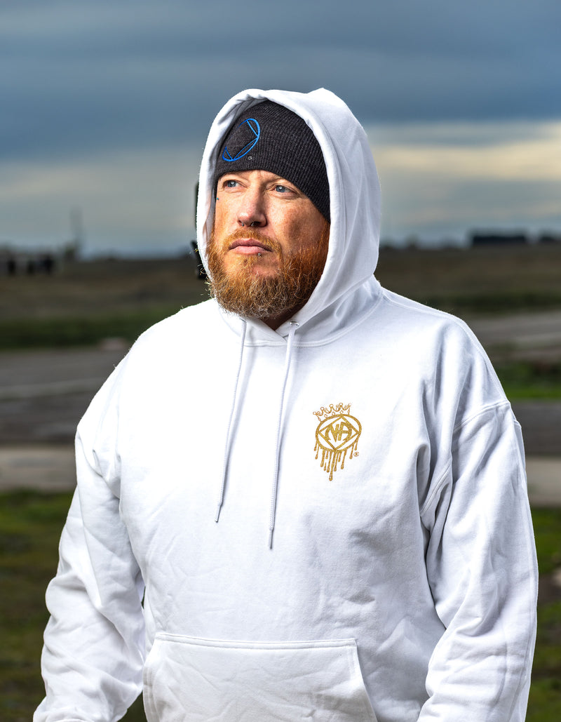 Load image into Gallery viewer, Man wearing a white hoodie with a logo, standing outdoors with a cloudy sky.