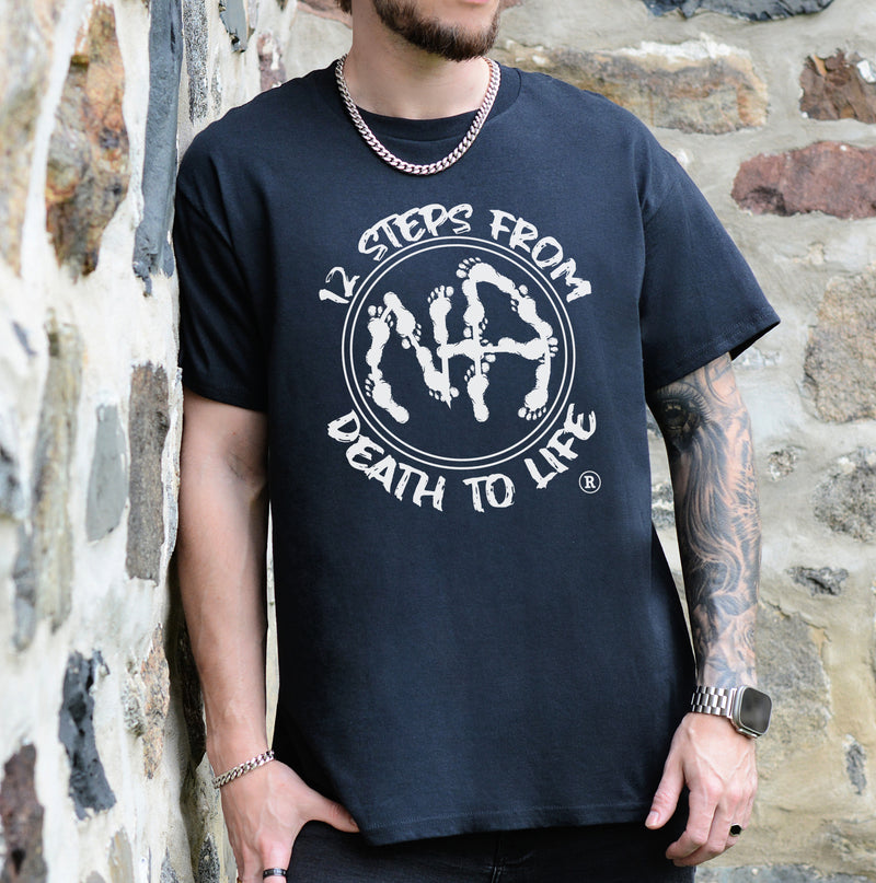 Load image into Gallery viewer, Person wearing a black t-shirt with a white graphic design against a stone wall background
