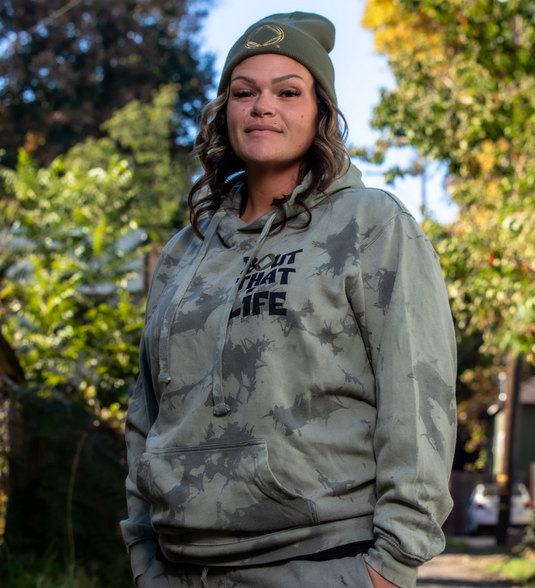 Person wearing a camouflage hoodie with text outdoors