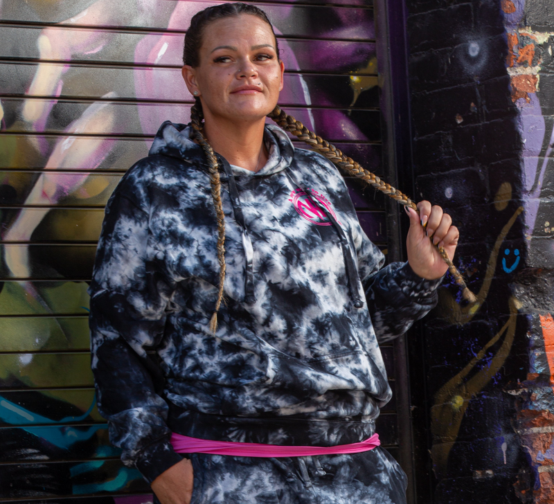 Load image into Gallery viewer, Woman wearing a tie-dye hoodie and shorts with pink accents in front of a graffiti-covered wall.
