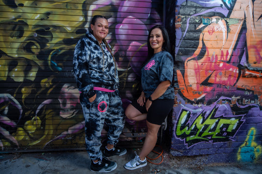Two women posing in front of a colorful graffiti wall.