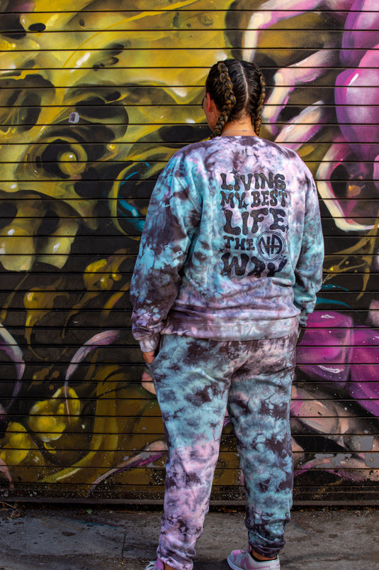 Person wearing a tie-dye outfit with text against a colorful graffiti wall.
