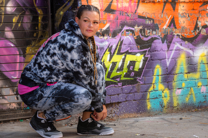 Load image into Gallery viewer, Person wearing a patterned jacket and pants in front of a colorful graffiti wall.

