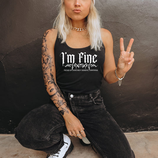Person wearing a black tank top with 'I'm fine' text, sitting against a dark wall.