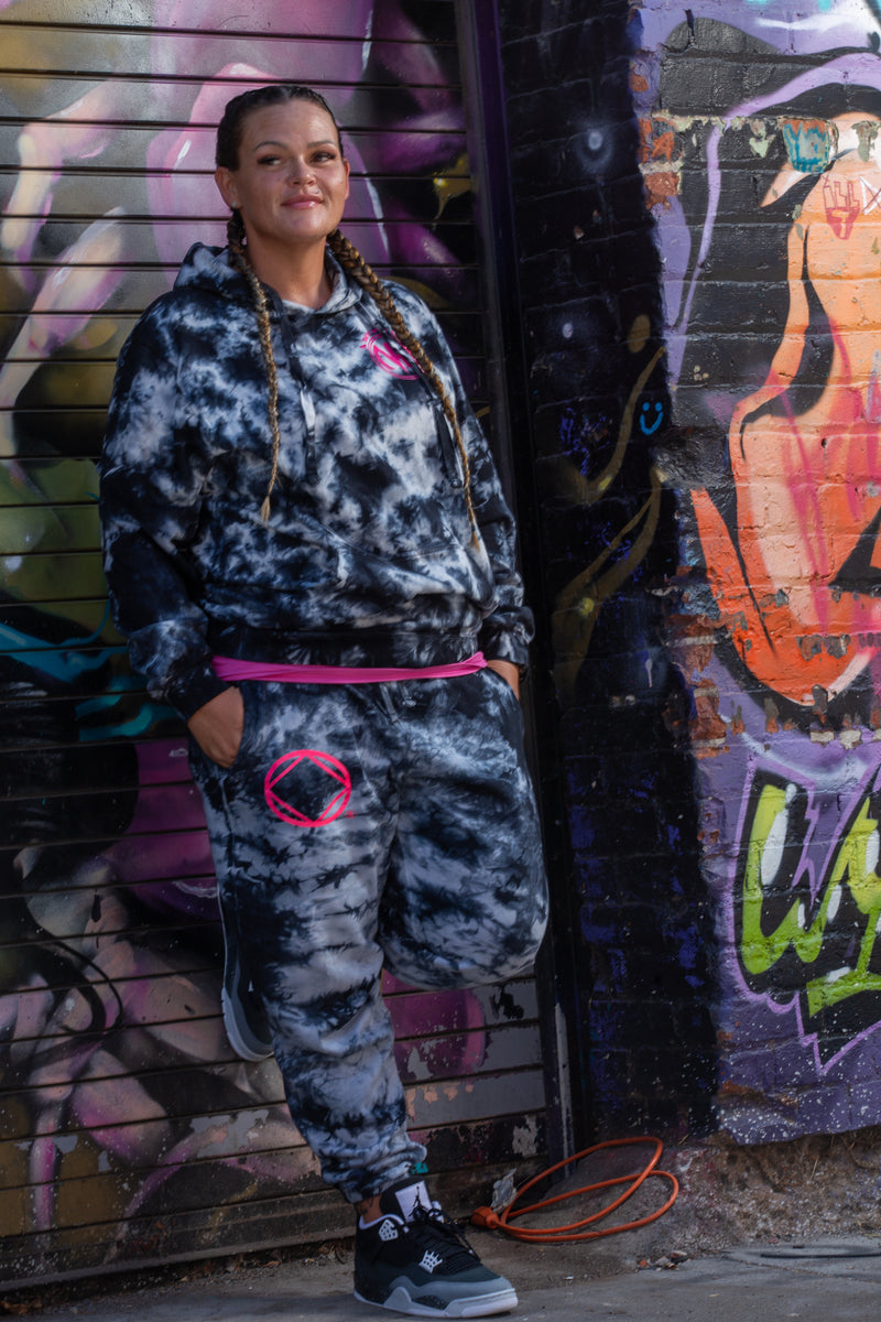 Load image into Gallery viewer, Person wearing a camouflage tracksuit with pink accents against a graffiti-covered wall.
