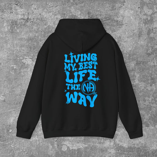 A person wearing a black hoodie with 'LIVING MY BEST LIFE THE NA WAY' printed in blue on the back.