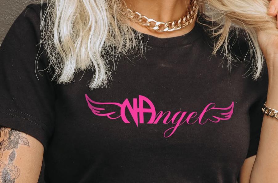 Female model with blonde hair, gold necklace and bracelet, and tattoos wearing a Gildan 64000L ladies softstyle tshirt in the color black with a centered chest print that says NAngel ( NA Angel)  in hot pink close up