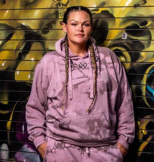 Person wearing a pink tie-dye hoodie in front of a colorful mural.