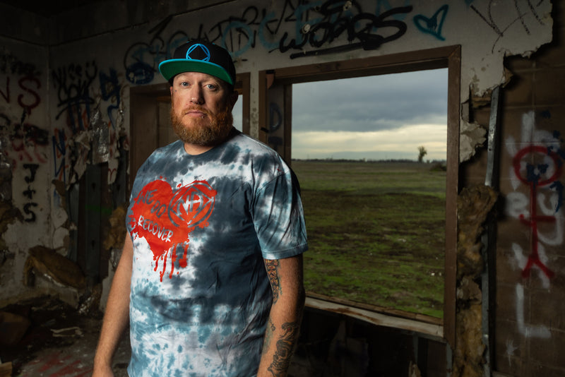 Load image into Gallery viewer, Man wearing a tie-dye shirt and cap in an abandoned building with graffiti.
