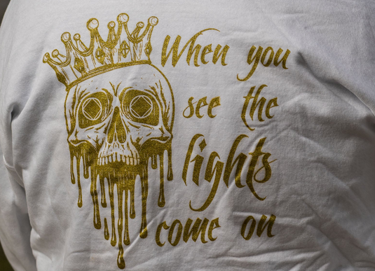 White shirt with gold skull and crown graphic and text 'When you see the lights come on'