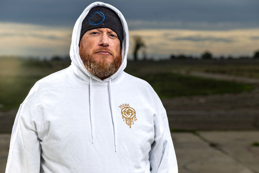 Man wearing a white hoodie with a logo, standing outdoors with a blurred background