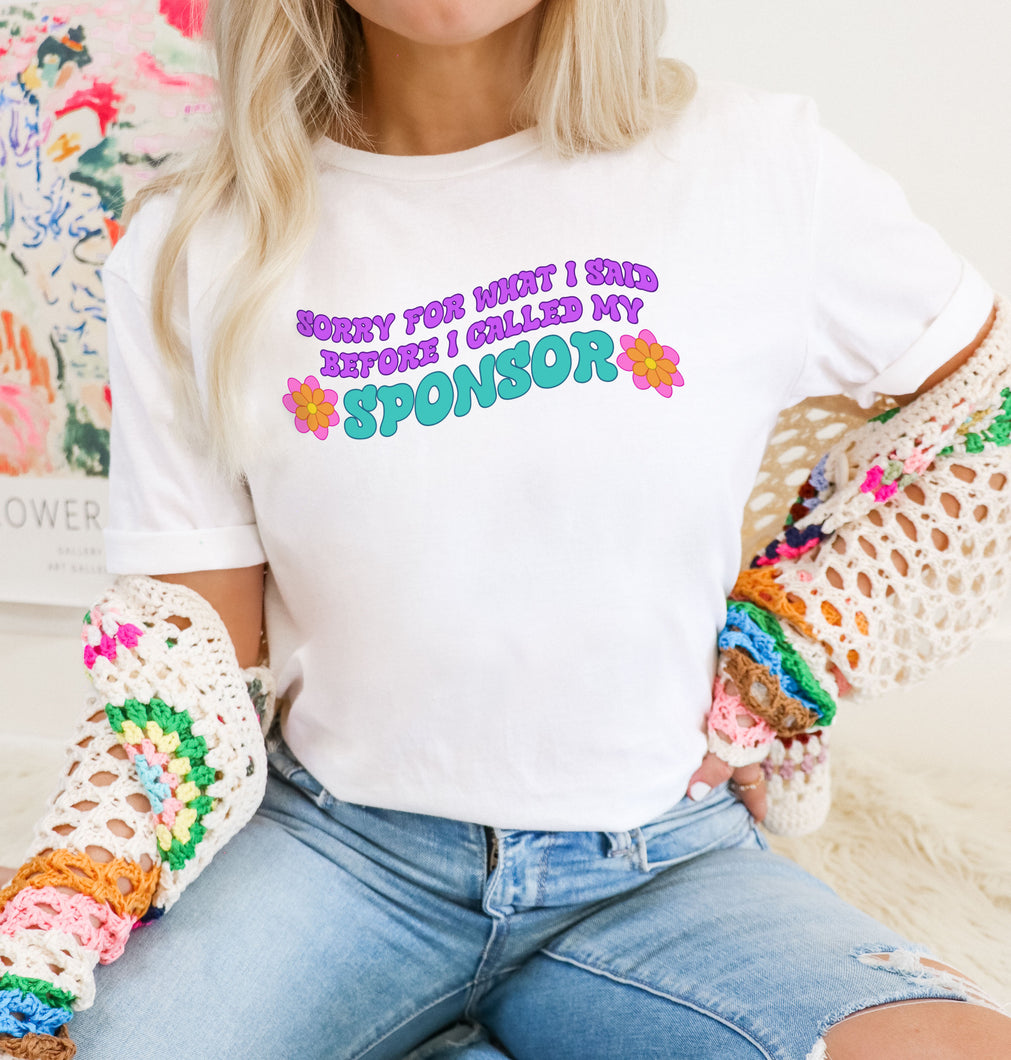 female model with blonde hair wearing white Gildan 64000L ringspun cotton tshirt with multi colored text that reads 'Sorry for what I said before I called my sponsor'with flowers and floral knitted cardigan.